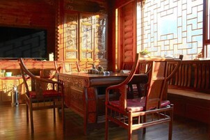 Un interior de madera con una mesa de comedor y sillas, una ventana con contraventanas decoradas, y un banco.