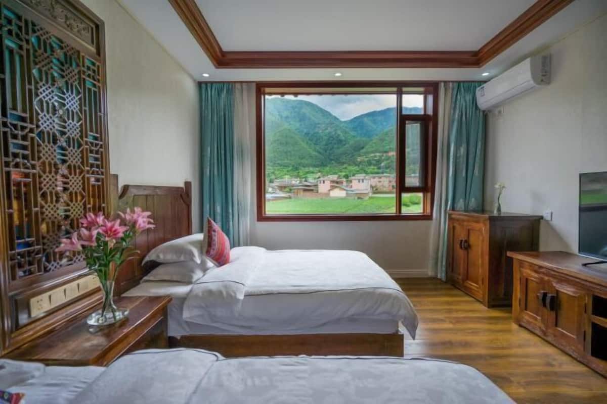 A bedroom with a bed, a nightstand, a TV, and a window with a mountain view.