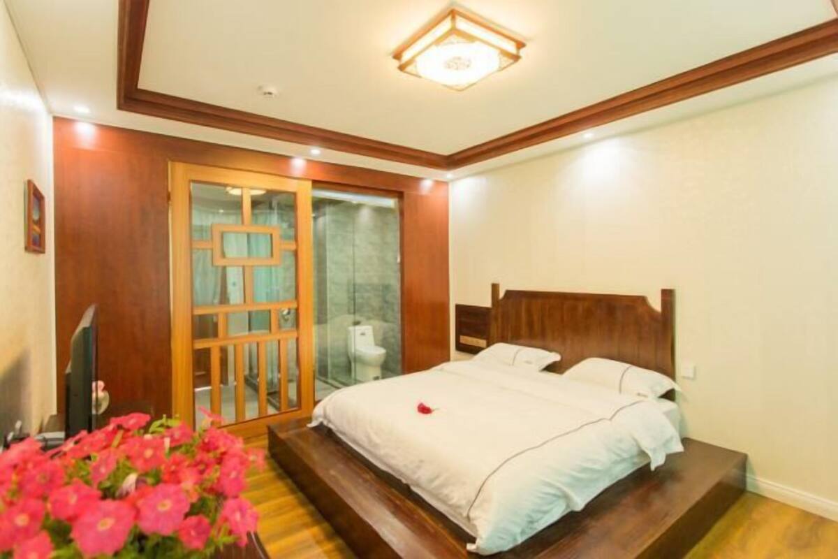 A bedroom with a wooden bed, a glass shower door, and a small bathroom.