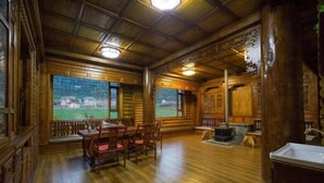 A log cabin interior with a dining area, a fireplace, and a view of a green landscape. - Lugu Manor Hotel (Ninglang)