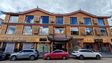 Un edificio de varios pisos con un estilo arquitectónico tradicional, que presenta una entrada central con un toldo decorativo. Hay varios coches estacionados al frente, y el edificio tiene varias señales que indican diferentes negocios o servicios.