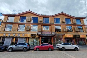 A multi-story building with a traditional architectural style, featuring a central entrance with a decorative awning. There are several cars parked in front, and the building has multiple signs indicating various businesses or services.