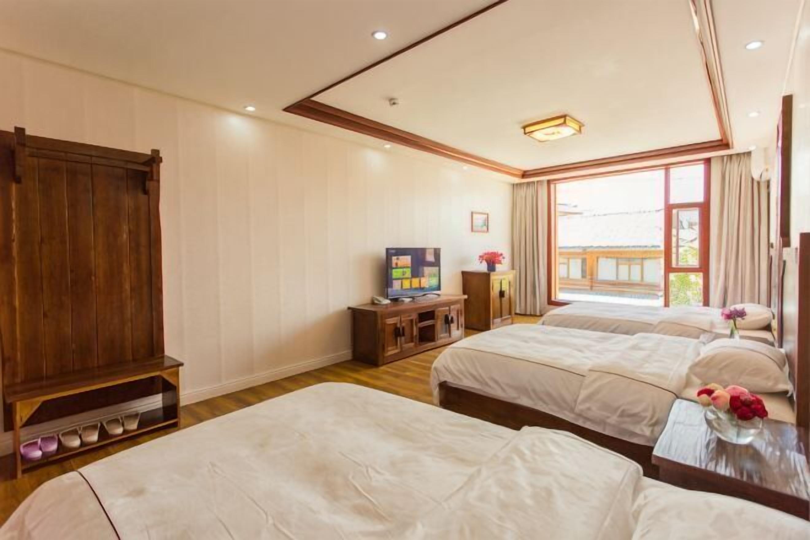 A hotel room with two beds, a wooden wardrobe, a television, and a large window.