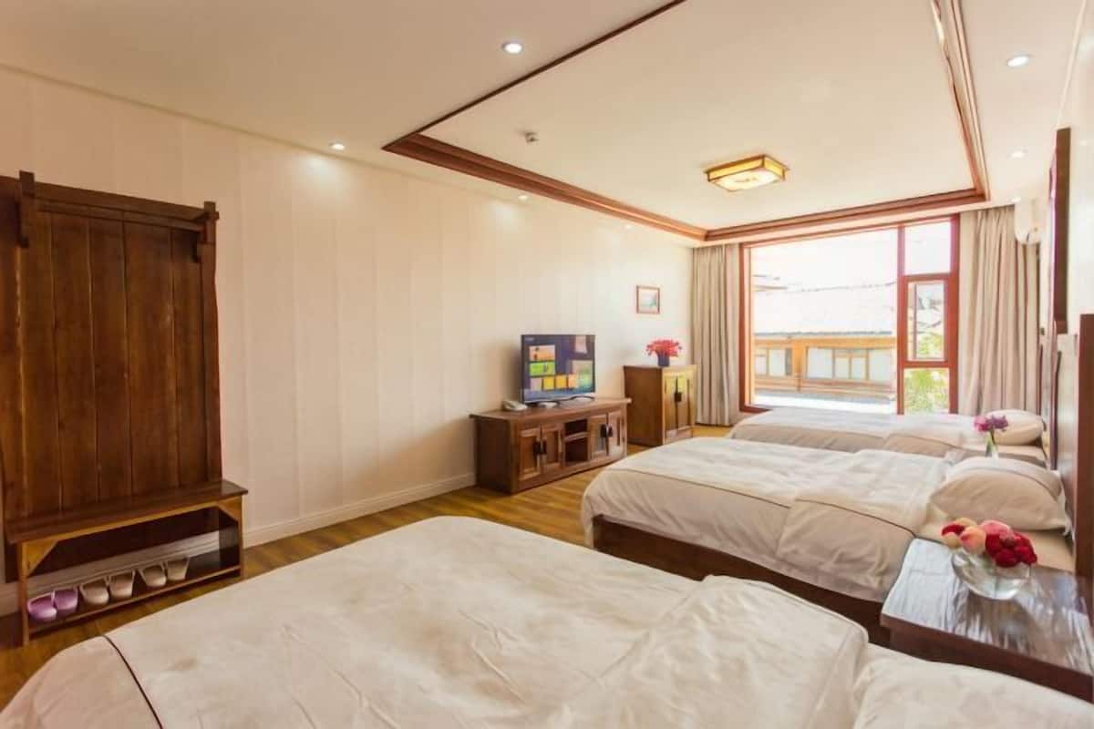 A hotel room with two beds, a wooden wardrobe, a television, and a large window.