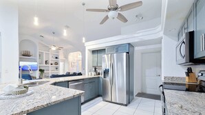 A modern kitchen with a central island, stainless steel appliances, and a ceiling fan.