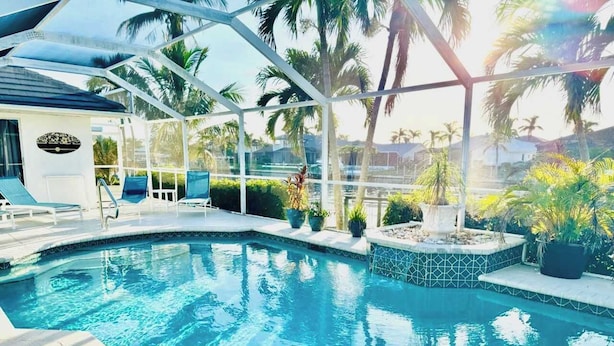 An indoor swimming pool with clear blue water, surrounded by lounge chairs and potted plants.