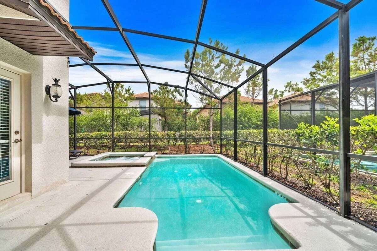 A swimming pool with a glass enclosure, surrounded by greenery and a clear sky.