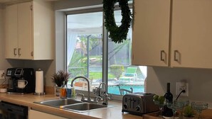 A modern kitchen with a large window, a coffee maker, a toaster, and a tray with glasses and a plant. - Hidden Secret Waterfront Retreat (Cape Coral)