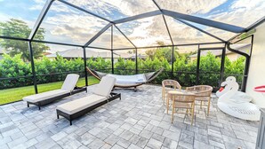 A covered outdoor patio with lounge chairs, a hammock, and a swan-shaped table. - Unwind in Paradise (Cape Coral)