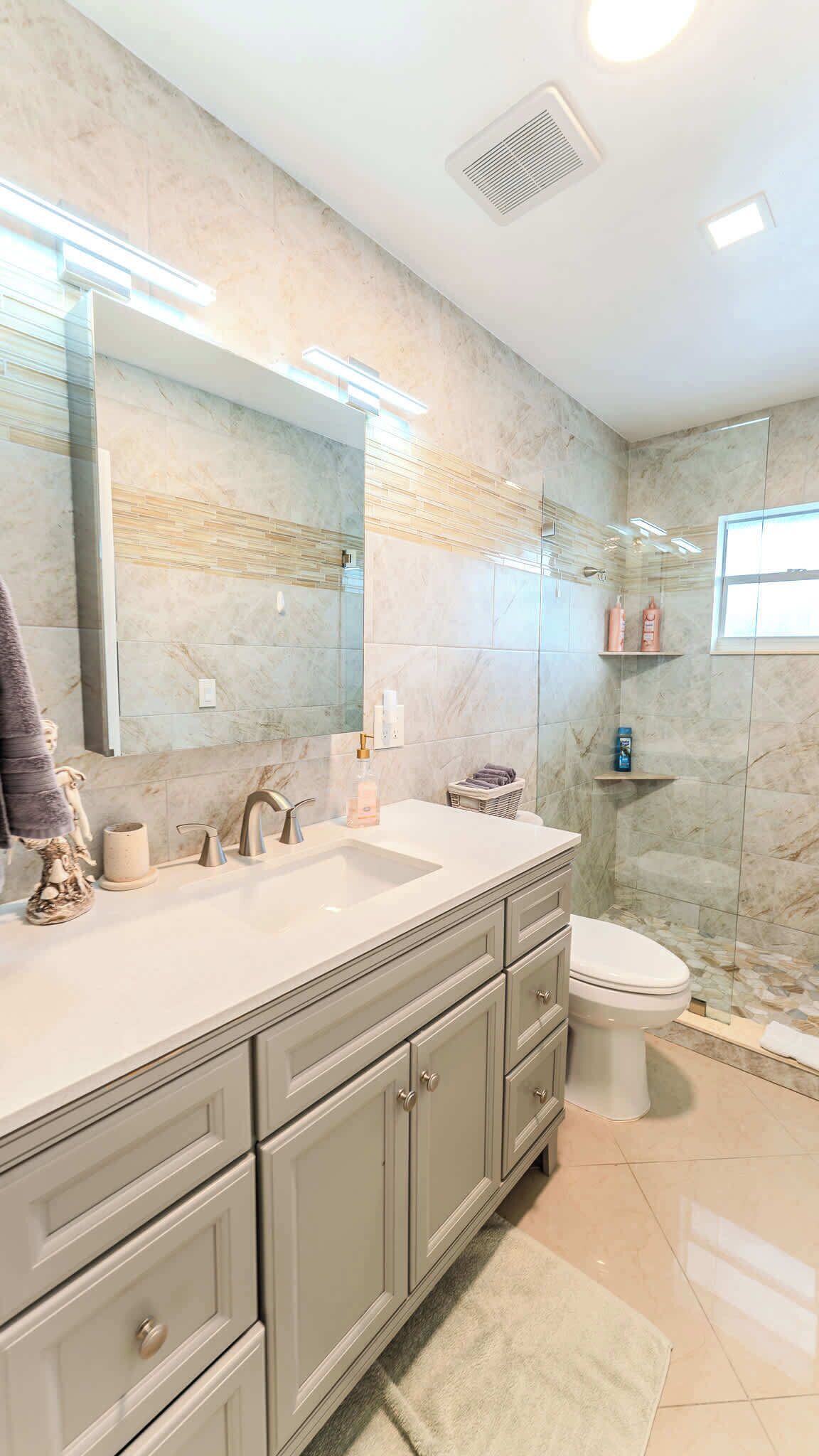 A modern bathroom with a large mirror, two sinks, a toilet, and a shower area.