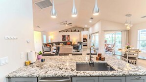 A modern kitchen with granite countertops, a stainless steel sink, and pendant lighting. - Unwind in Paradise (Cape Coral)