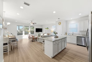 Una cocina moderna con armarios blancos, una isla central y un comedor con televisión y asientos.