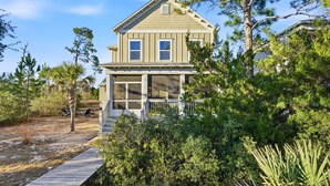 A two-story house with a porch, surrounded by dense greenery and a clear sky. - Spacious 4BR w/ Pool Access|Walk to Beach|Fire Pit (Port St. Joe)