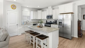 A modern kitchen with white cabinets, a stainless steel refrigerator, a microwave, and a coffee maker. - Spacious 4BR w/ Pool Access|Walk to Beach|Fire Pit (Port St. Joe)