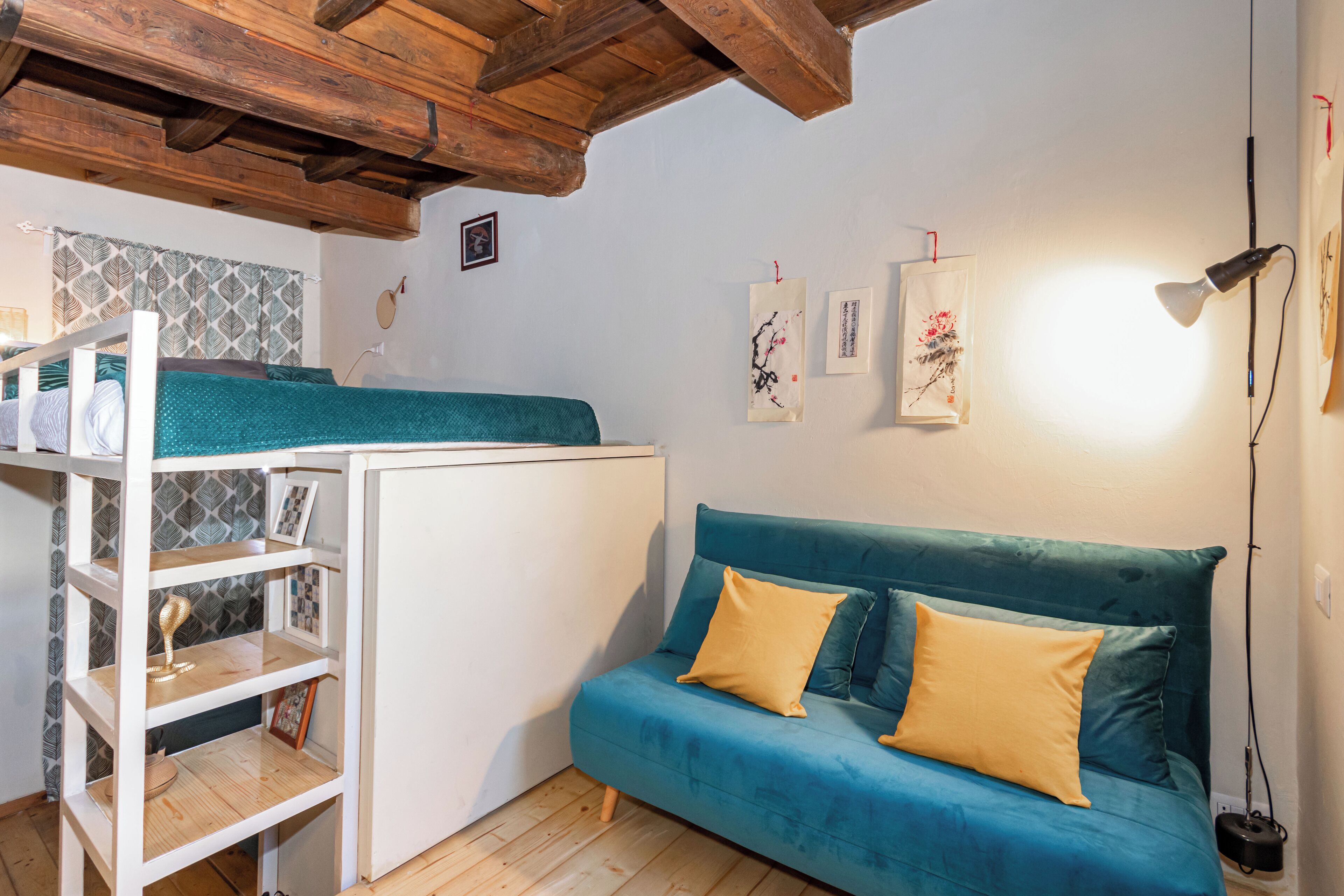 Una habitación compacta con una cama litera, un sofá con cojines, un estante blanco y obras de arte en las paredes.