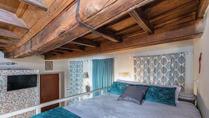 Un dormitorio con techo de madera, una cama con ropa de cama a rayas, un televisor en la pared y cortinas estampadas.