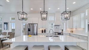 Cucina spaziosa con un'ampia isola, mobili bianchi e illuminazione a sospensione.