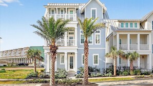 Una casa sulla spiaggia su due piani con un balcone, palme e cielo sereno.