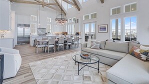 A spacious living area with a high ceiling, wooden beams, a dining area, and large windows offering views of the city. - Summer Wind 217 TEA (Port Aransas)