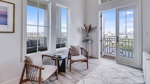 A spacious balcony with large windows, a wooden floor, and a view of the city. - Summer Wind 217 TEA (Port Aransas)