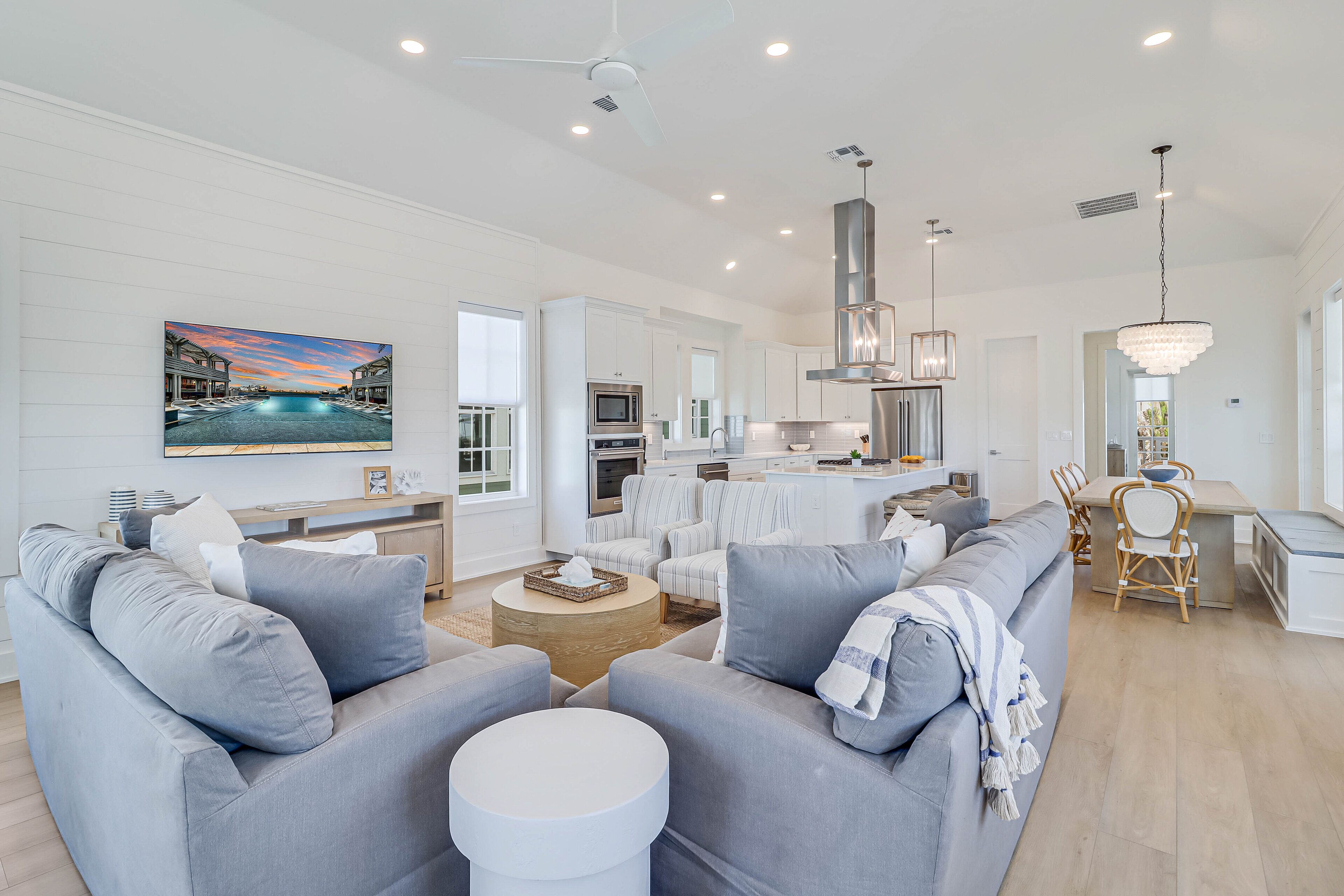 A spacious living room with a grey sofa set, a coffee table, and a painting of a sunset over a pool.
