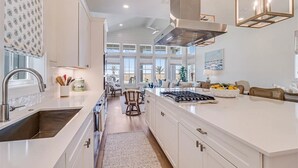 Una cocina moderna con armarios blancos, una isla grande, electrodomésticos de acero inoxidable y vistas al área de comedor.