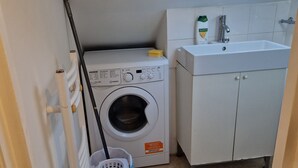 A compact laundry room with a front-loading washing machine, a sink, and a window above the machine. - A studio overbooking the city  (London)