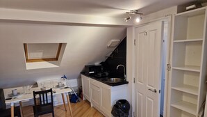 A compact kitchen with a dining area, a black trash bin, and a white door. - A studio overbooking the city  (London)
