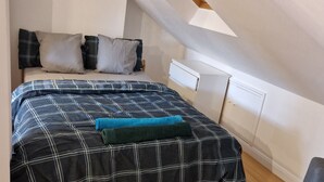 A bedroom with a sloped ceiling, a bed with a plaid bedspread, and a wooden floor. - A studio overbooking the city  (London)