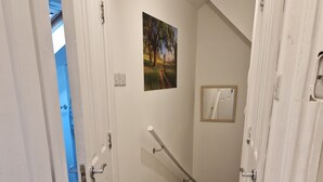 A narrow hallway with white doors, a handrail, and a small painting on the wall. - A studio overbooking the city  (London)