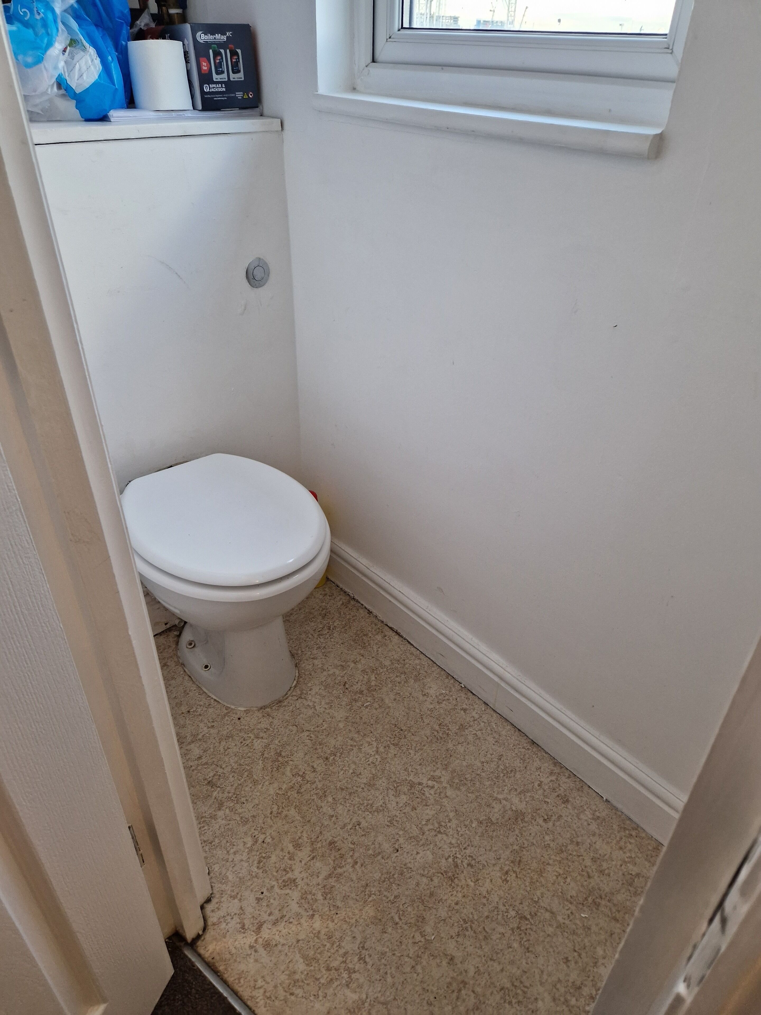 Een kleine, witte badkamer met een toilet, een raam boven het toilet en een witte muur.