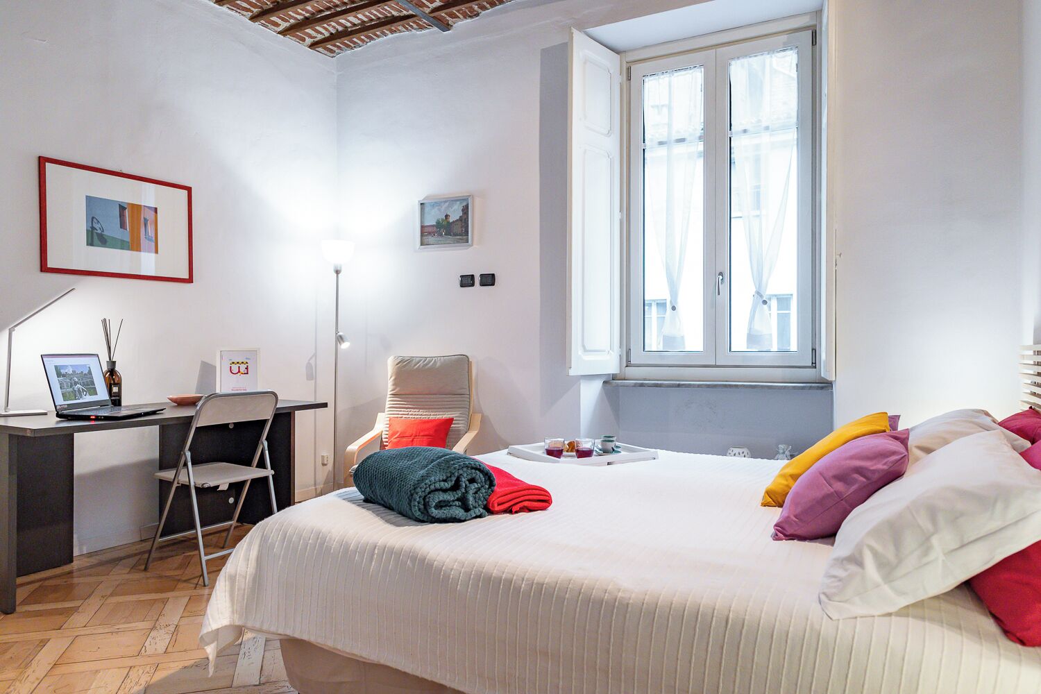 A bedroom with a bed, a desk, a chair, a window, and a painting on the wall.