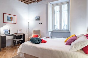 Une chambre à coucher avec un lit, un bureau, une chaise, une fenêtre et un tableau accroché au mur.