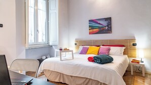 A bedroom with a bed, a desk, a chair, a window, and a painting on the wall. - Apple House al Duomo by Wonderful Italy (Turin)