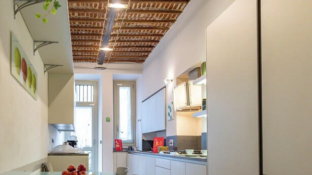 A modern kitchen with white cabinets, a glass dining table with apples, and a brick ceiling. - Apple House al Duomo by Wonderful Italy (Turin)