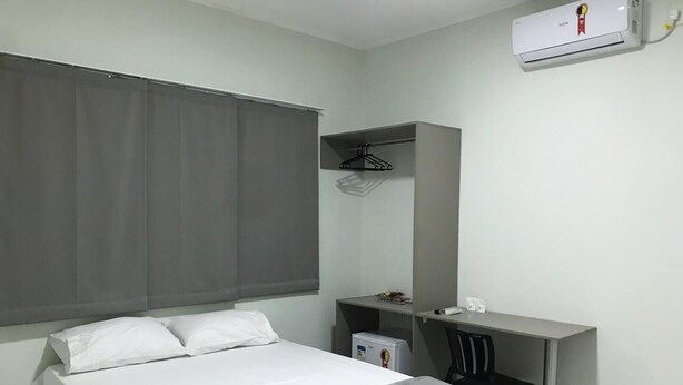 A bedroom with a bed, a desk, a chair, a small fridge, and an air conditioning unit. - Comfort Hotel  (Porangatu)