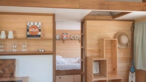 A cozy room with a wooden bunk bed, a small desk with a laptop, and shelves with various items including a hat and a book.