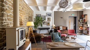 A cozy living room with a stone wall, a wooden table, a fireplace, and a bookshelf.