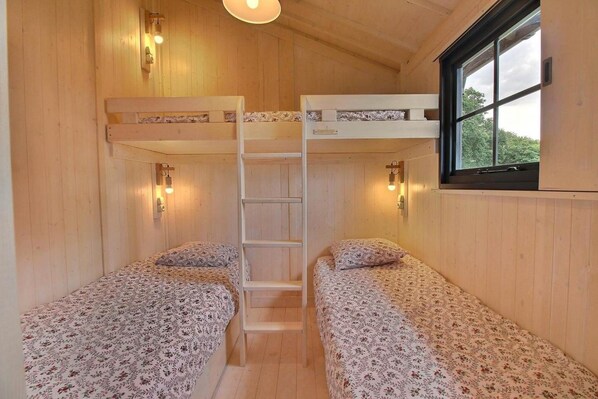 A cabin with two bunk beds, wooden walls, a ladder, and a window with a view.
