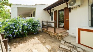 A white building with a stone foundation, wooden steps leading to a covered patio, and a fan mounted on the exterior wall.