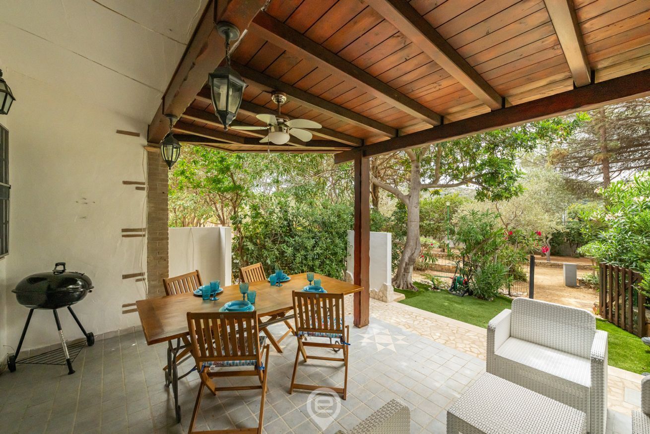 A covered patio area with a wooden table and chairs, a ceiling fan, and a grill.