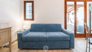 A room with a blue sofa, a wooden cabinet, a small table with a lamp, and a window with bars.