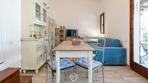 A dining area with a wooden table, blue patterned chairs, a cabinet with glass doors, a television, and a blue sofa.