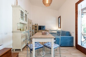 Un coin repas avec une table en bois, des chaises à motifs bleus, un meuble avec des portes en verre, un téléviseur et un canapé bleu.