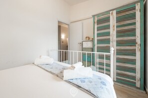 Une petite pièce propre, avec un lit, une armoire blanche et une porte dotée de volets verts.