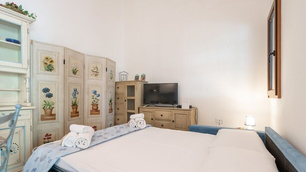 A hotel room with a bed, a TV, a dresser, and a cabinet with floral decorations.