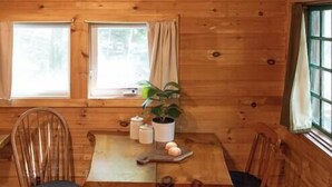 L’intérieur d’un chalet en bois, avec une table à manger, deux chaises, une plante en pot et une fenêtre.