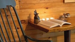 L’intérieur d’un chalet en bois, avec une chaise à ossature métallique, une petite table ornée de bougies et un livre.