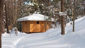 Een houten hutje met een sneeuwbedekte dak, omringd door bomen en een besneeerd landschap.