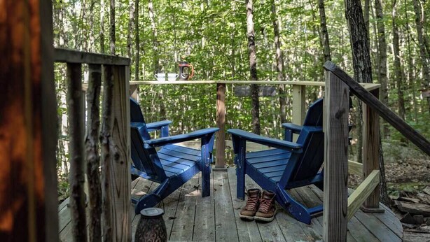 Een houten terras met twee blauwe stoelen en een paar laarzen.